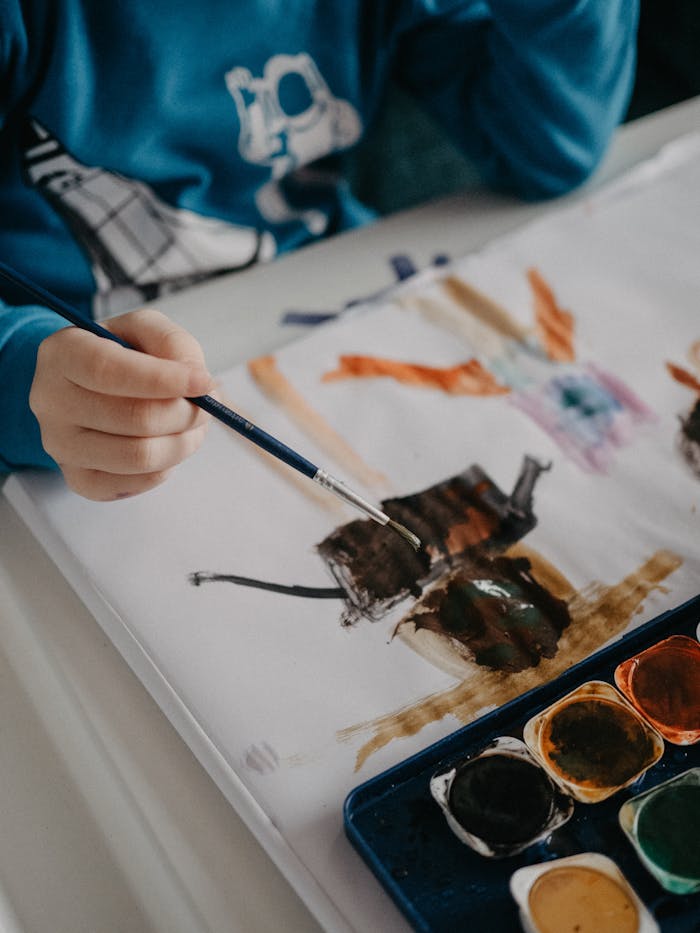 A young child creating artwork with watercolors on white paper.